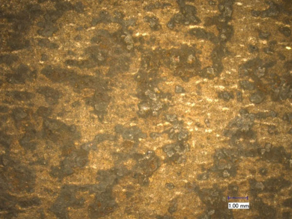 This figure shows the virgin A588 steel surface observed under visible light with an optical microscope after the doping and extraction process. The scale bar in the image is 0.04 inches (1 millimeter long). Rust is visible on the steel surface after the doping and extraction process.