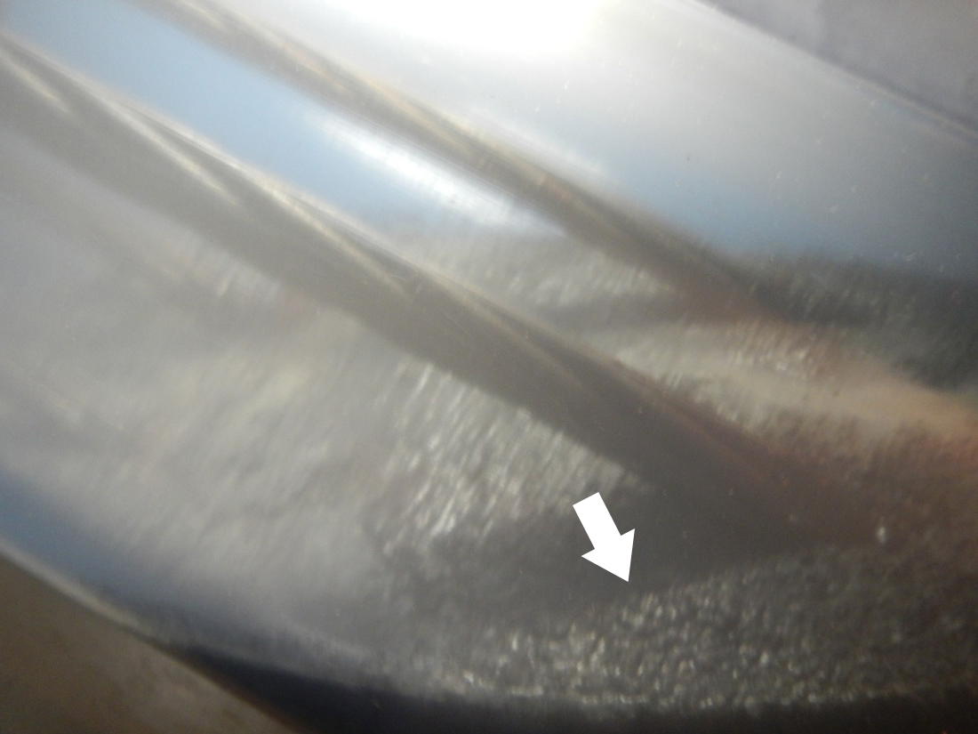 Figure 159. Photo. Void condition of 0.4 percent chloride specimen. This photo shows stressed strands in the void of 0.4 percent chloride multi-strand specimen 1 week after recharging water was added to the void. Black deposit is visible on the void/grout interface where stressed strands passed through. A white arrow points to unknown deposit material.