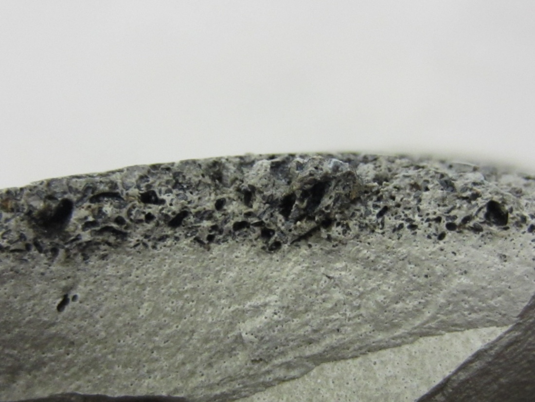 Figure 223. Photo. Cross section of the grout piece shown in figure 222. This photo shows a cross-sectional view of the same piece of grout shown in figure 222. A porous layer and black particles are visible.