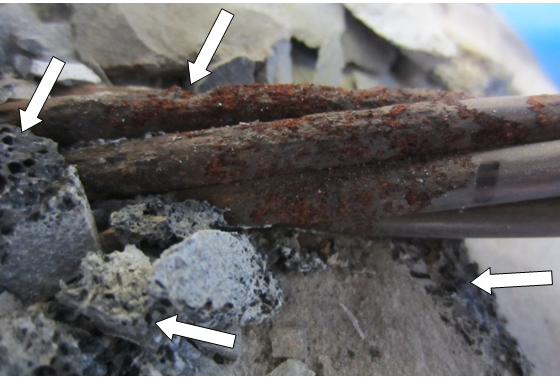Figure 226. Photo. Another exposed strand at the void/grout interface of 0.4 percent chloride multi-strand specimen. This photo shows stressed strand of 0.4 percent chloride multi-strand specimen that experienced significant section loss. Black deposit is indicated by white arrows.