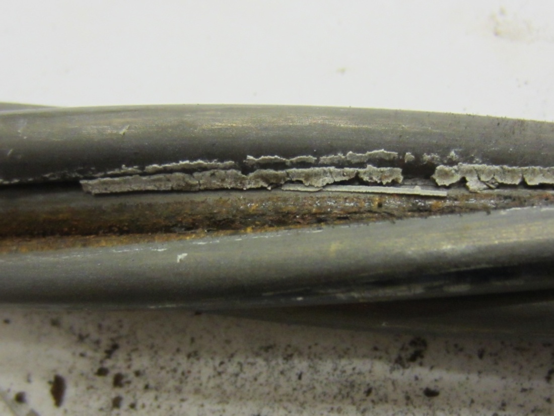 Figure 235. Photo. Grout fragment found inside an interstice surrounded by corroding wires. This photo shows a hardened grout layer stuck in an interstice when an outer wire was removed. Moderately corroded wires are visible.