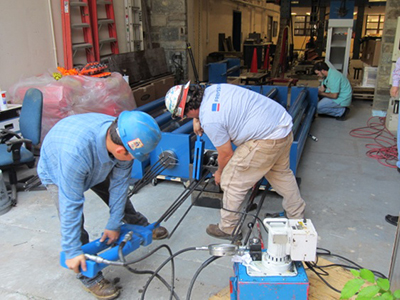 Figure 30. Photo. Stressing of multi-strand specimens. This photo shows strand stressing for multi-strand specimens. Two workers are pulling a strand using a hydraulic jack.