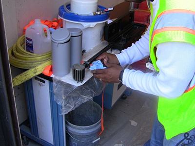 Figure 34. Photo. In-situ grout testing. This photo shows a worker taking a unit weight measurement of a grout mix as part of the standardized in-situ grout testing.