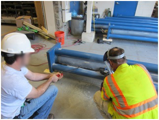 Figure 68. Photo. Cutting the clear duct to expose grout. This photo shows a destructive dismantling process. Workers are seen cutting the clear duct.