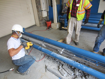 Figure 69. Photo. Chipping grout to expose PT strands. This photo shows a worker removing two duct halves and chipping the grout away to expose the post-tensioned (PT) strands
