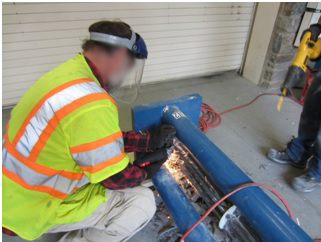 Figure 71. Photo. Cutting PT strands near the lower anchor bearing plate. This photo shows a worker cutting a strand near the lower anchor plate after grout was completely removed.