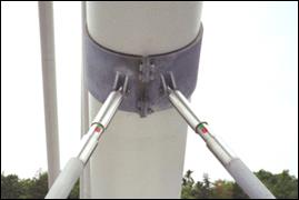 This photo shows a close up view of a pair of dampers attached to a cable by the galvanized steel damper bracket. They are attached to the cable at slight opposite angles, so that as they extend to the median slab by their respective steel support shafts, they form an isosceles triangle.