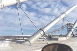 This photo was taken from the roadway showing the base of a cable. It features a side view of a pair of dampers and their steel support shafts and where they are anchored to the galvanized steel damper bracket at the top and the median slab at the bottom.