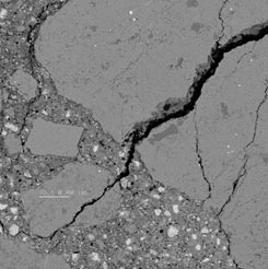 This is a photo of the microstructure of one of the test mortars (ON1) taken in the scanning electron microscope in the backscattered mode and at the magnification of 100x. The photo shows a large piece of aggregate that occupies about half of the picture (starting from the northeast corner) and a few smaller pieces of aggregate surrounded by the hydrated cement paste located in the remaining (southwest and west) part of the picture. The photo also shows a crack that splits the larger aggregate in two parts. The crack originates near the southwest corner of the picture and runs more or less diagonally, becoming wider near the northeast corner of the picture.