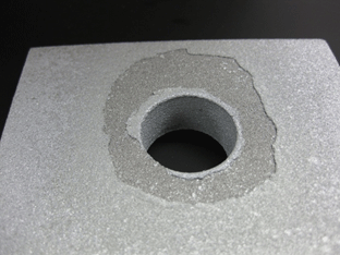 Figure 4. Photo. Typical post-test faying surface of unsealed TSC. This photo shows the tested faying surface of one plate from a compression test specimen. Only the upper half of the plate with the hole is shown. The perimeter of the hole (a rough circular shape twice the diameter of the drilled hole) is missing the thermal spray coating.