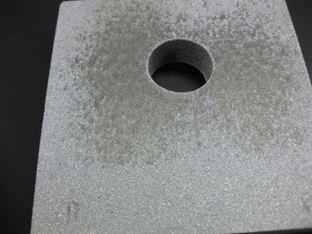 Figure 5. Photo. Typical post-test faying surface of sealed TSC. This photo shows the tested faying surface of one plate from a compression test specimen. For a distance roughly one hole diameter away from the drilled hole perimeter, the thermal spray coating has a duller grey appearance than the rest of the TSC and is considerable smoother in appearance.