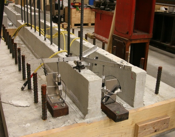 Figure 7. Photograph. Displacement measurement via three LVDTs. The photograph shows that steel bar displacement was measured at location of approximately two inches above the top surface of UHPC strip. Three LVDTs were arranged in 120-degree angle.