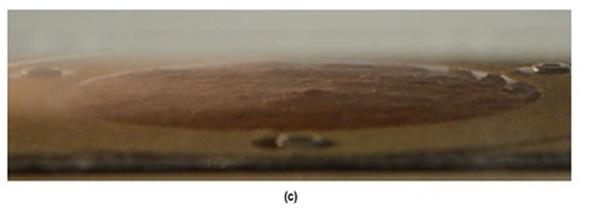 In this photo, a progression of erosion changes are seen. For the lower bed shear stress of 0.10 lbf/ft2 (4.9 Pa), there was no cloudiness (image a). The soil was eroded in small lumps over the soil surface. When the bed shear stress was increased to 0.21 lbf/ft2 (10 Pa), increasing cloudiness was observed, and larger lumps of soil were entrained in the flow (image b). When the bed shear stress was increased to 0.27 lbf/ft2 (13.1 Pa), the cloudiness increased, and the erosion rate increased. At this higher shear stress, shallow grooves appeared on the soil surface along the flow direction (image c).