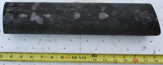 Figure 4. Photo. Received unthreaded sample after cleaning. This photo shows a bar of steel. A ruler in the foreground shows the overall length is approximately 15 inches. The width of the bar appears to be about 3 inches. Figure 4. Photo. Received unthreaded sample after cleaning. This photo shows a bar of steel. A ruler in the foreground shows the overall length is approximately 15 inches. The width of the bar appears to be about 3 inches.