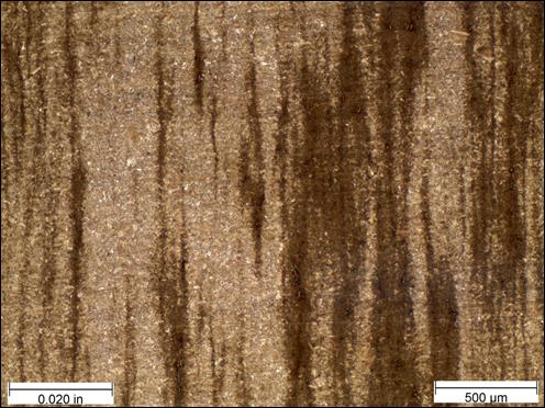 Figure 27. Photo. Micrograph near rod center etched with Marshall’s reagent at 50x magnification. This photo shows a micrograph that was taken near the center of the threaded rod at a magnification of 50x and viewed under bright field illumination. The sample was etched with Marshall’s reagent. A scale bar with a length of 0.020 inches is shown in the lower left corner of the photo, and a scale bar with a length of 500 micrometers is shown in the lower right corner. The sample shows vertical banding of dark and light brown regions. A large band of dark brown is present in the right-center portion of the photo, while a large band of light brown is present in the left-center portion. Smaller bands of light and dark brown are present throughout the photo.