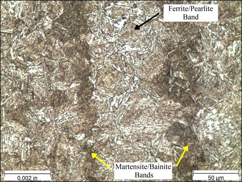 Figure 29. Photo. Micrograph near rod center etched with Marshall’s reagent at 500x magnification. This photo shows a micrograph that was taken near the center of the threaded rod at a magnification of 500x and viewed under bright field illumination. The sample was etched with Marshall’s reagent. A scale bar with a length of 0.002 inches is shown in the lower left corner of the photo, and a scale bar with a length of 50 micrometers is shown in the lower right corner. The micrograph shows alternating vertical bands of two distinctly different microstructures. The dark brown region appears as a needle-like martensite and bainite structure. The lighter brown bands have regions of ferrite that have an appearance similar to fish scales and regions of pearlite that appear as small pockets of parallel lines. The ferrite and pearlite regions are much less dense than the martensite regions. The bands of ferrite/pearlite and martensite/<br /> bainite are labeled on the photo. Figure 29. Photo. Micrograph near rod center etched with Marshall’s reagent at 500x magnification. This photo shows a micrograph that was taken near the center of the threaded rod at a magnification of 500x and viewed under bright field illumination. The sample was etched with Marshall’s reagent. A scale bar with a length of 0.002 inches is shown in the lower left corner of the photo, and a scale bar with a length of 50 micrometers is shown in the lower right corner. The micrograph shows alternating vertical bands of two distinctly different microstructures. The dark brown region appears as a needle-like martensite and bainite structure. The lighter brown bands have regions of ferrite that have an appearance similar to fish scales and regions of pearlite that appear as small pockets of parallel lines. The ferrite and pearlite regions are much less dense than the martensite regions. The bands of ferrite/pearlite and martensite/<br /> bainite are labeled on the photo.