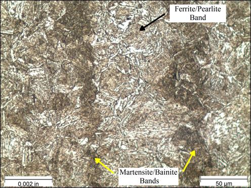 Figure 29. Photo. Micrograph near rod center etched with Marshall’s reagent at 500x magnification. This photo shows a micrograph that was taken near the center of the threaded rod at a magnification of 500x and viewed under bright field illumination. The sample was etched with Marshall’s reagent. A scale bar with a length of 0.002 inches is shown in the lower left corner of the photo, and a scale bar with a length of 50 micrometers is shown in the lower right corner. The micrograph shows alternating vertical bands of two distinctly different microstructures. The dark brown region appears as a needle-like martensite and bainite structure. The lighter brown bands have regions of ferrite that have an appearance similar to fish scales and regions of pearlite that appear as small pockets of parallel lines. The ferrite and pearlite regions are much less dense than the martensite regions. The bands of ferrite/pearlite and martensite/<br /> bainite are labeled on the photo.