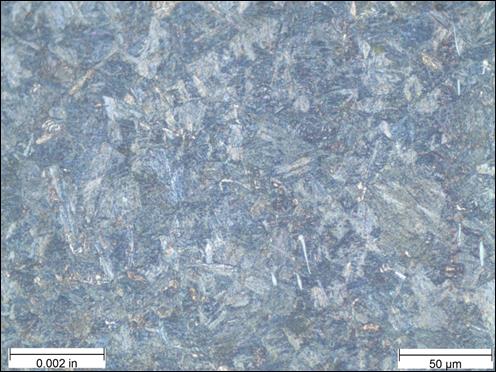 Figure 30. Photo. Micrograph near thread root etched with 10-percent potassium metabisulfite at 500x magnification. This photo shows a micrograph that was taken near the thread root of the threaded rod at a magnification of 500x and viewed under polarized light. The sample was etched with 10-percent potassium metabisulfite. A scale bar with a length of 0.002 inches is shown in the lower left corner of the photo, and a scale bar with a length of 50 micrometers is shown in the lower right corner. The microstructure in the photo is mostly uniform and appears as a needle-like martensite structure. The microstructure color varies over a range of blues, with the majority being dark blue. There are speckles of brown and gray patches interspersed throughout the photo.