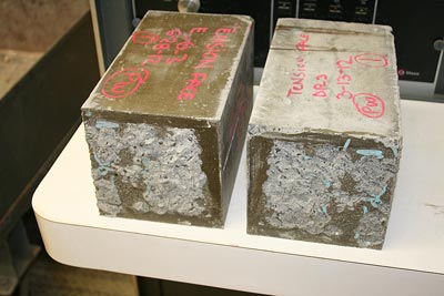 The photo shows partial concrete substrate failure from a bond flexural test using 6- by 6- by 21-inch (152.4- by 152.4- by 533.4-mm) prism specimens, with “chunks” of concrete remaining on the grout side of the interface.