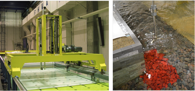 This photo shows the automated flume carriage positioned above the flume on the left and the acoustic Doppler velocimeter probe extended into the water on the right. The probe is positioned near the corner of the model abutment above a section of rock at the base of the abutment that is colored. They are colored to highlight the rocks when they move during the experiments.