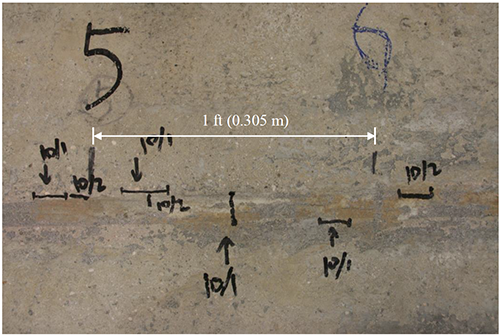 This photo shows some of the cracking that occurred to the partial-depth conventionally grouted connection in the process of thermal loading. A 1-ft (0.305-m) length is shown as comparison to the cracks. Seven cracks are visible. The cracks occurred mainly at the interface between the grout and box beams and are between about 0.5 and 2 inches (12.7 and 50.8 mm). The average length is 1.2 inch (30.7 mm).