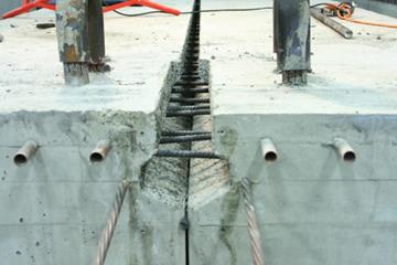 This photo shows beams aligned with partial-depth ultra-high performance concrete (UHPC) connections. They have been positioned and aligned but are not yet grouted together. The size and shape of the connection is visible, and the reinforcement extending from each beam can be seen extending between the beams. The reinforcement toward the end of the beam appears to be nearly in contact, while reinforcement more toward the center is not.