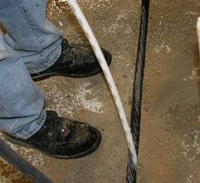 This photo shows a connection using conventional grout that is being wetted before the grout is cast. A worker is placing a white hose into the shear key connection. The connection and the concrete surrounding it are visibly wet.
