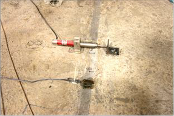 This photo shows the installation of a linear variable differential transformer (LVDT) and a transverse strain gauge on the top of the connection. The LVDT is mounted on one beam, measuring against a steel angle on the second beam. The strain gauge is positioned parallel to the LVDT on the grouted connection.