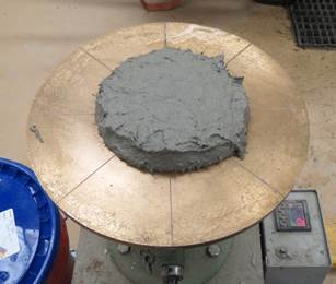Figure 5. This photo shows a thixotropic UHPC-class material during an ASTM C1437 flow table test after removal of miniature slump cone. The photo shows that the UHPC has not spread far across the brass flow table. The flow diameter is approximately 4.5 in (114 mm). 