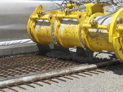 Figure 13. This figure shows a photo of the UHPC placement machine actively placing the UHPC overlay on a prepared section of bridge deck. The prepared bridge deck section has been formed, and a layer of steel reinforcing bars has been placed.
