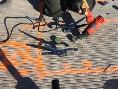 Figure 26. This figure shows a photo from in-situ bond testing on the Laporte Road bridge. This photo shows preparation of the bond test locations and installation of the test discs. This photo shows two test discs after being glued to the UHPC overlay surface. A heat gun is being used to accelerate adhesive curing.