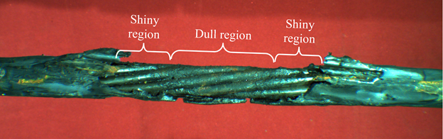 This photo shows a sheathed strand oriented horizontally. The sheathing has been melted away in the central portion of the strand, exposing the wires. In the very center of the strand, a bracket is used to distinguish an area called &ldquo;Dull region&rdquo; that extends about two strand diameters. To the left and right of the dull region extending for about one strand diameter is an area annotated as &ldquo;Shiny region.&rdquo;