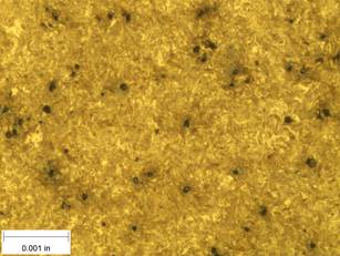 A scale bar is provided in the picture showing a dimension of 0.001 inch, and therefore the field of view is approximately 0.005 inch wide and 0.0038 inch tall. The image comprises two types of microstructures: light and dark. Both microstructures appear to be randomly distributed through the image and have grain sizes on the order of 0.0002 inch. The image also contains a random distribution of round inclusions, also around 0.0002 inch.