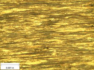 A scale bar is provided in the picture showing a dimension of 0.001 inch, and therefore the field of view is approximately 0.005 inch wide and 0.0038 inch tall. The image comprises two types of microstructures: light and dark. Both microstructures are elongated across the width of the image and alternately layered through the height of the image. A larger proportion of the image comprises the darker microstructure.