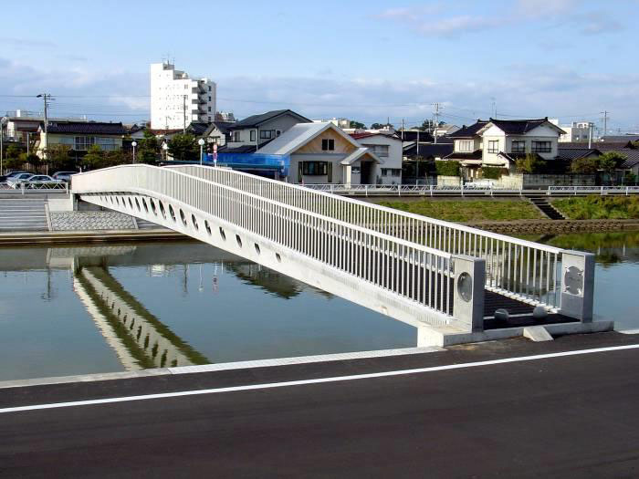 The photograph shows a side view of the single span pedestrian bridge taken from the river bank.