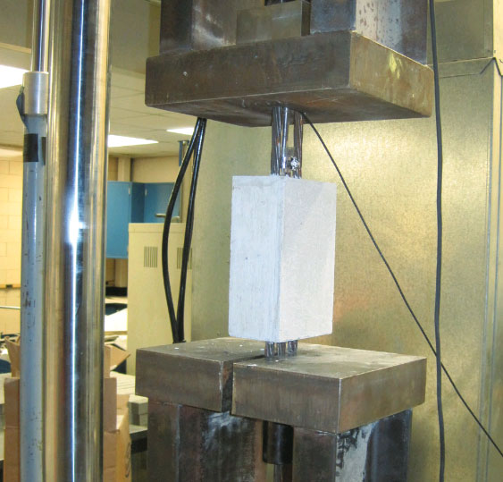 This figure shows the testing of an 8-inch (20.3 cm) long test specimen. The upper and lower loading platens are visible along with the strand chucks and the displacement transducer that measured strand slippage.