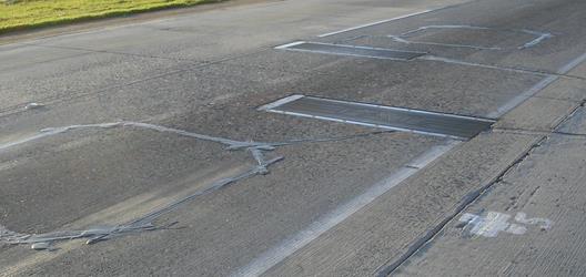 Figure 3. Photo. Staggered bending plate installation and inductive loops. This photo shows a road surface where a bending plate weigh-in-motion system consisting of four weighpads has been installed. Two of the weighpads are staggered left to right, while the other two weighpads are side-by-side down the length of the roadway. A sealant has been used on the road, leaving a tar-like substance along the edges of the weighpads and forming slightly raised outlines.