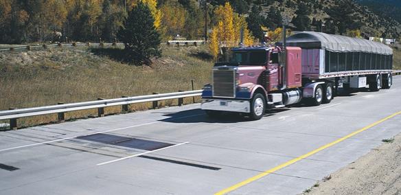 Figure 4. Photo. Inline configuration of load cell-based weight sensors. This photo shows two lanes of a highway. Weighpad sensors have been installed in the road surface. An 18-wheel truck is approaching the camera from the top-right side of the photo in the right lane.