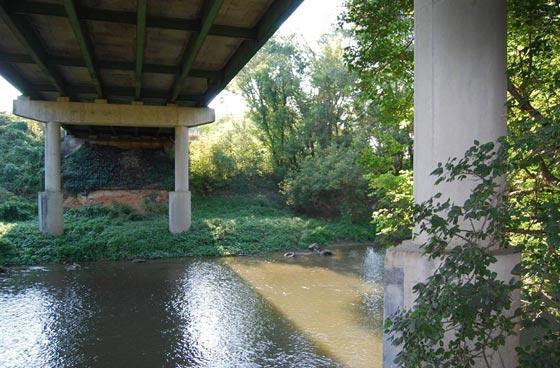 This ground-level photo shows the underside of the I-70 Antietam Creek bridge and a set of supports of one span. Antietam Creek is in the foreground.