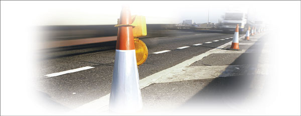 Photograph taken at road-level of placed along a stretch of road.  A truck is in the foreground driving in the open lane.