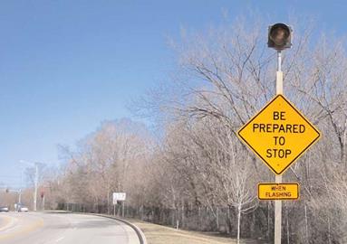 This photo shows an upstream advance warning sign for a dynamic reversible left turn (DRLT). The warning sign reads “Reversible Left Turn Ahead.” A smaller sign below it reads “WHEN FLASHING,” and a signal can be seen at the top of the sign.