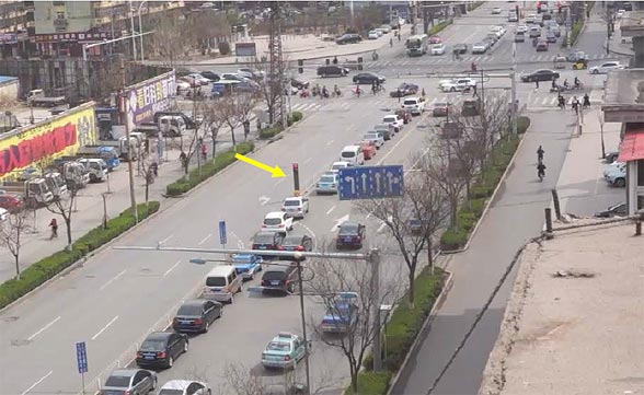 This photo focuses on the northbound approach to a signalized intersection in China. In the middle of this photo is a presignal that controls entry to two contraflow left-turn (CLT) pockets. Approximately 600 ft of the northbound approach lanes are visible within the photo. The queue of left-turning vehicles is so long that it extends beyond the bottom edge of the photo (i.e., beyond 600 ft). There are 17 vehicles visibly queued up in the left-turn lane before reaching the bottom edge of the photo. The presignal is located in the middle of the visible queue length 