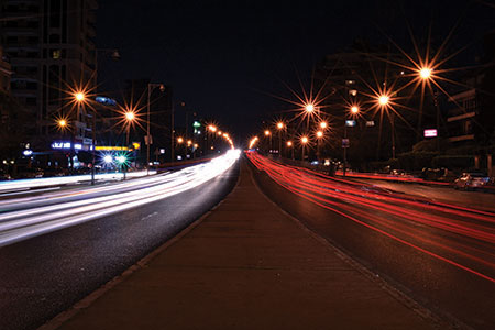 A time-elapsed photo of a highway at night with headlights and taillights streaming into the distance as cars travel toward and away from the camera.