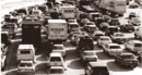 This photograph shows at least seven lanes of traffic on an interstate. All lanes are full, bumper to bumper. There are both cars and trucks on the highway.