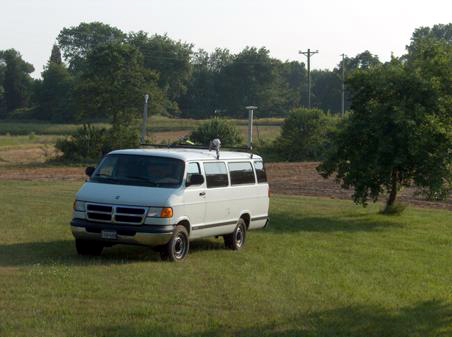 Figure 23. Photo. Van configuration used for driver analysis on U.S. Route 15. Picture of a large white van with two antennas mounted on top.  The van is facing toward the lower left hand corner of the photo. On the left side of the van toward the front is a HA-NDGPS antenna; on the right side of the van is mounted the GPS antenna.
