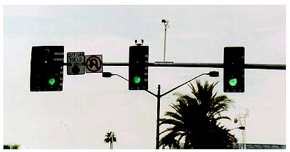 Figure 1-6. Overhead camera mounting on a mast arm as typically used to provide imagery to a VIP for arterial signal control. Photograph shows a camera in a weather-proof housing mounted on a vertical pole that extends upright from a signal mast arm; it provides imagery to a video image processor system.