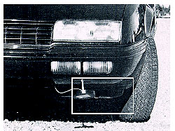 Figure 3-17. Transmitter mounted under a vehicle identifies it to a subsurface inductive loop detector. A photograph of a disk shaped transmitter that can be programmed to transmit a unique vehicle ID code to an inductive-loop detector (ILD) electronics unit is shown mounted under the front bumper of an automobile.