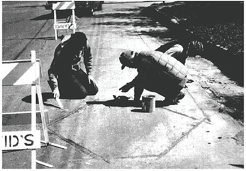 Figure 5-30. Finishing sealant application. Photograph of two men removing excess sealant from pavement. 
