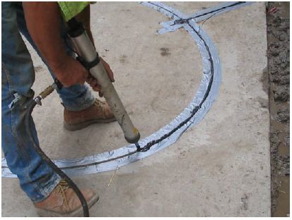 Figure 5-50. Placing sealant in sawcut. The technician uses a pressure gun with a pointed tubular end to inject the correct amount of sealant into the saw cut.