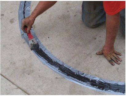 Figure 5-51. Removing excess sealant. The technician kneels on the pavement and uses a scraper to remove the excess sealant form above the sawcut and the removable tape.